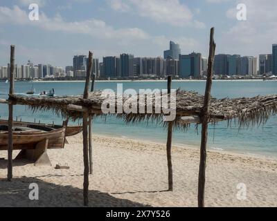 Plage avec des cabanes traditionnelles au premier plan et une ligne d'horizon moderne en arrière-plan, ligne d'horizon d'une ville au bord de la mer avec des palmiers au premier plan, AB Banque D'Images