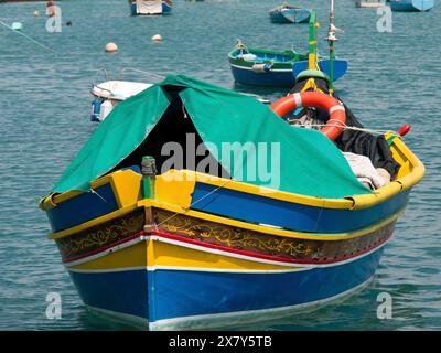 Un bateau de pêche coloré avec couverture en tissu vert et bouée de sauvetage à l'ancre, de nombreux bateaux de pêche colorés dans un port en Méditerranée, Marsaxlokk, M. Banque D'Images