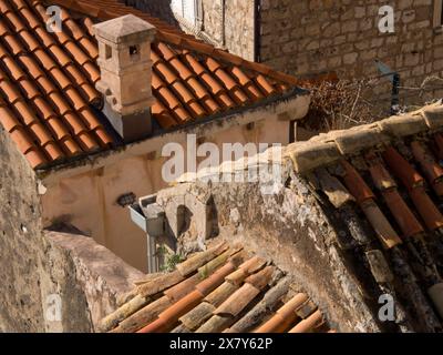 Gros plan des toits rustiques avec des murs en pierre et une cheminée, mettant en évidence les tuiles rouges et les textures dans la lumière du soleil, les toits de tuiles rouges d'une ville historique par Banque D'Images