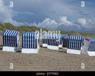 Un groupe de chaises de plage bleues et blanches se dresse sur la plage devant des dunes herbeuses et un ciel nuageux, des chaises de plage rayées bleues et blanches sur la mer Banque D'Images