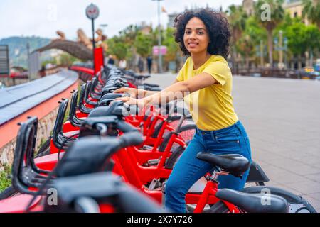 Portrait d'une jeune femme latine souriant à la caméra tout en utilisant le service public de location de vélos Banque D'Images