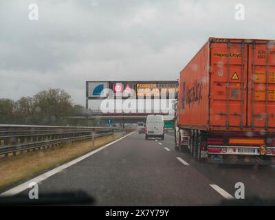 Scène d'autoroute avec un camion et une camionnette, temps pluvieux, viaduc en vue et un panneau d'avertissement électronique, jour de pluie sur l'autoroute A1, Piacenza, Italie, Europ Banque D'Images
