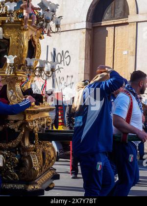 Statue ornée portée par des gens lors d'une procession religieuse dans une rue aux murs couverts de graffitis, Catane, italie, 3 février 2024, 3 jours fès Banque D'Images