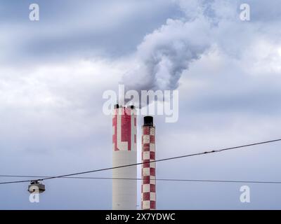 Cheminées industrielles à Bâle, Suisse, émettant de la fumée blanche, motif rayé rouge et blanc, câble utilitaire avec un lampadaire, ciel nuageux. Banque D'Images