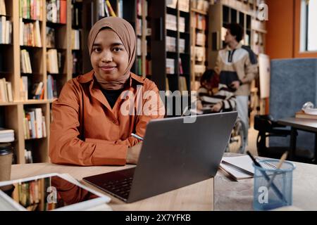 Jeune fille musulmane moderne portant le hijab assis au bureau dans la bibliothèque universitaire étudiant avec l'utilisation d'un ordinateur portable, espace de copie Banque D'Images