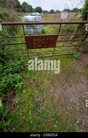 Une porte rouillée de cinq bars dans l'Essex rural avec un avis presque illisible protège un réservoir en plastique géant abandonné dans le champ au-delà .. élevage soigneux. Banque D'Images