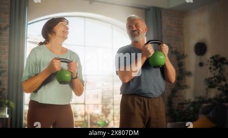 Couple d'âge moyen inspiré faisant des exercices matinaux et Kettlebell Workout ensemble à la maison dans le salon ensoleillé. Concept de mode de vie sain, condition physique, loisirs, objectifs de couple et retraite. Banque D'Images