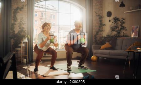 Heureux couple Senior faisant des exercices du matin et Kettlebell entraînement ensemble à la maison dans le salon ensoleillé. Mode de vie sain, remise en forme, loisirs, objectifs de couple, bien-être et retraite. Banque D'Images