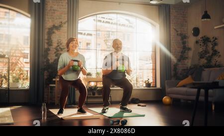 Heureux couple Senior faisant des exercices du matin et Kettlebell entraînement ensemble à la maison dans le salon ensoleillé. Concept de mode de vie sain, condition physique, loisirs, objectifs de couple, bien-être et retraite. Banque D'Images