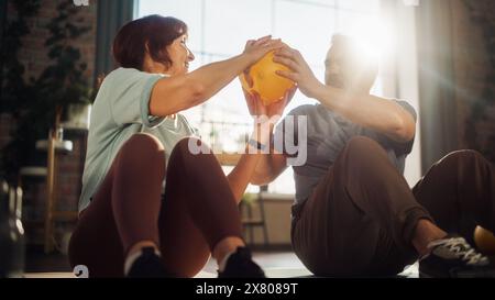 Couple senior heureux faisant des exercices de renforcement de noyau ensemble à la maison dans le salon ensoleillé. L'homme et la femme seniors se motivent mutuellement pour être la santé. Concept Lifestyle and Fitness. Banque D'Images