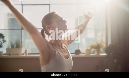 Jeune femme athlétique exerçant, pratiquant la méditation le matin dans son lumineux salon ensoleillé de Loft Apartment. Mode de vie sain, Fitness, bien-être et concept de pleine conscience. Banque D'Images