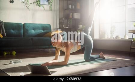 Athlétique jeune femme exercice, étirement et faire du yoga tout en suivant la vidéo d'entraînement sur ordinateur portable. Belle femme en vêtements de sport pratiquant différentes poses Asana sur le tapis. Banque D'Images