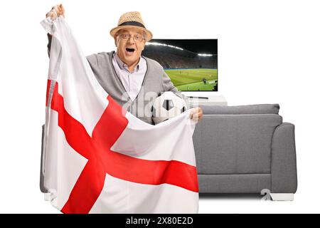 Fan de football âgé excité tenant un drapeau anglais devant un canapé et une télévision isolés sur fond blanc Banque D'Images