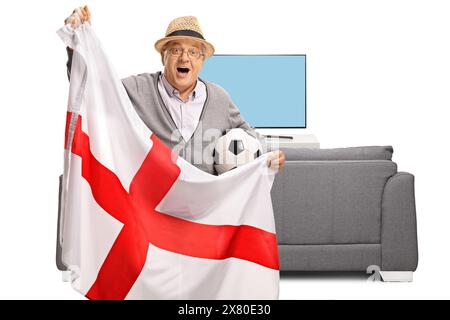 Fan de football âgé tenant un drapeau anglais devant un canapé et une télévision isolés sur fond blanc Banque D'Images