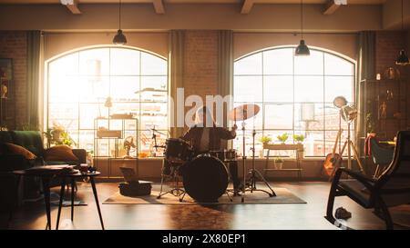 Beau jeune batteur jouant à une répétition de Band, faisant des tricks avec des baguettes de batterie. Apprendre Drum Solo sur les tambours et les cymbales dans le salon ensoleillé de l'élégant appartement loft. Banque D'Images