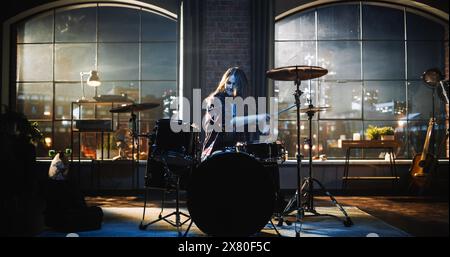 Jeune femme jouant de la batterie pendant une répétition de Band dans un studio de loft pendant une session de soirée ou de nuit. Drummer Girl pratiquant avant un concert live sur Big Stage avec le public. Banque D'Images