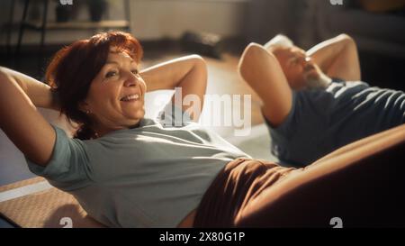 Couple senior faisant des exercices de renforcement de base et des exercices de crunches ensemble à la maison dans Sunny Living Room. Mode de vie sain, remise en forme, loisirs, bien-être et retraite heureuse. Banque D'Images