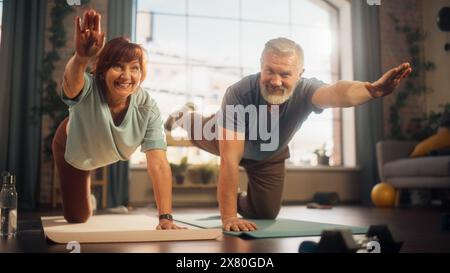 Portrait d'un couple senior faisant des exercices d'étirement de gymnastique et de yoga ensemble à la maison le matin ensoleillé. Concept de mode de vie sain, condition physique, loisirs, objectifs de couple, bien-être et retraite. Banque D'Images