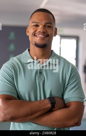 Physiothérapeute masculin biracial debout avec les bras croisés, souriant au centre de rééducation de gymnastique Banque D'Images