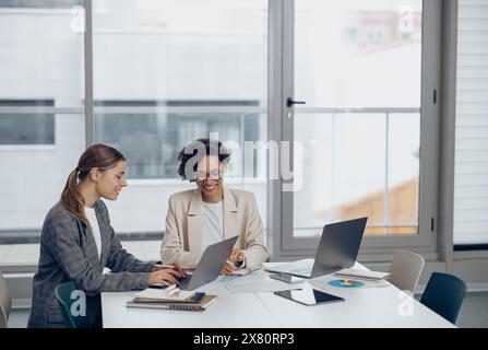 Deux collègues féminines concentrées travaillant sur le projet ensemble et utilisent un ordinateur portable assis dans le bureau Banque D'Images