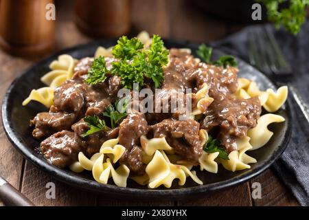 Stroganoff de bœuf avec nouilles aux œufs garnies de persil sur une assiette noire Banque D'Images