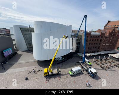 Stralsund, Allemagne. 22 mai 2024. Les employés de l'entreprise de nettoyage de façades FassadenFix de Halle/Saale nettoient la façade du musée faite de grands panneaux de construction navale en acier. Les 360 panneaux en acier incurvés blancs de l'Ozeaneum couvrent une superficie d'environ 3800 mètres carrés et atteignent des hauteurs allant jusqu'à 24 mètres. Huit employés de FassadenFix effectuent le nettoyage en utilisant quatre bus de lavage et trois plates-formes spéciales - dont certaines mesurent jusqu'à 51 mètres de haut. Crédit : Stefan Sauer/dpa/ZB/dpa/Alamy Live News Banque D'Images