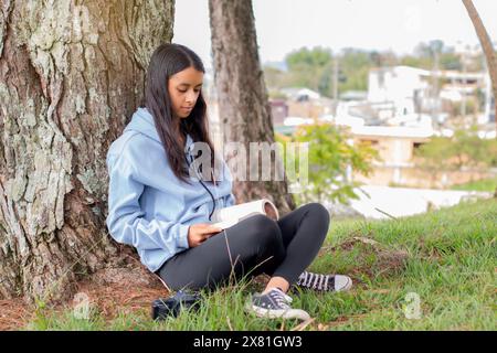 style de vie : jeune latina lisant un livre assis à côté d'un arbre Banque D'Images