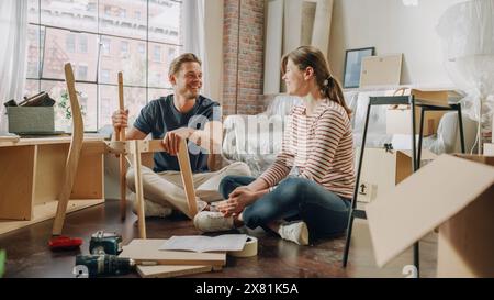 Famille déménagement et rénovation de la maison : couple heureux assemble des meubles ensemble, petite amie lit les instructions et petit ami les suit avec une certaine Force. Nouvel appartement pour les jeunes partenaires amoureux Banque D'Images