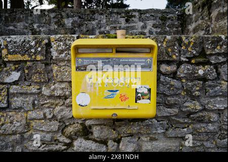 Boîte aux lettres publique jaune vintage, altérée et ornée de stickers délavés, montée sur un ancien mur de pierre à Carcassonne. Banque D'Images