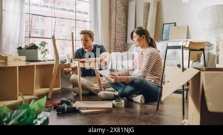 Famille déménagement et rénovation de la maison : couple heureux assemble des meubles ensemble, petite amie lit les instructions et petit ami les suit avec une certaine Force. Nouvel appartement pour les jeunes partenaires amoureux Banque D'Images