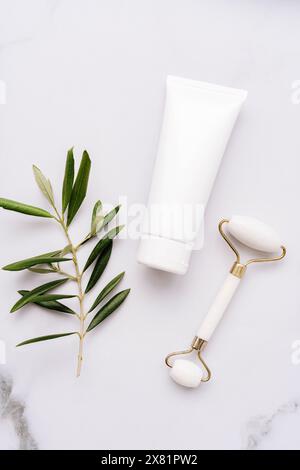 Gros plan du tube en plastique blanc sans étiquette et rouleau facial sur fond de table en marbre blanc. Concept minimal de bouteille de crème pour le visage, gel, baume Banque D'Images