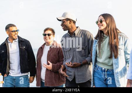 Amis multiethniques marchant et riant à l'extérieur - profiter d'un moment décontracté et joyeux - sourire et bavarder - groupe de jeunes adultes, l'amitié et Banque D'Images