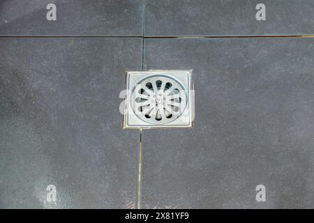 Le couvercle de drain en métal sur les carreaux de sol noirs dans la salle de douche, vue avant pour l'espace de copie. Banque D'Images