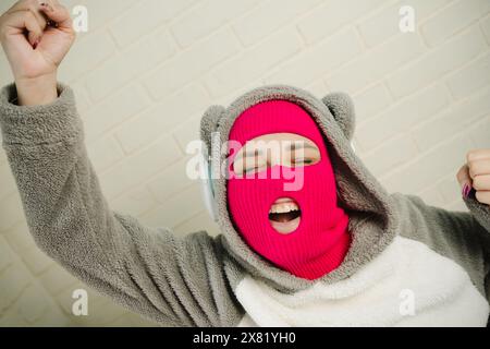 Femme en Balaclava rose dansant contre un mur de briques blanches Banque D'Images