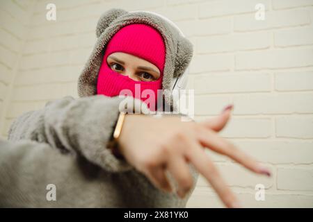 Femme en Balaclava rose dansant contre un mur de briques blanches Banque D'Images