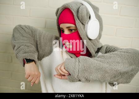 Femme en Balaclava rose dansant contre un mur de briques blanches Banque D'Images