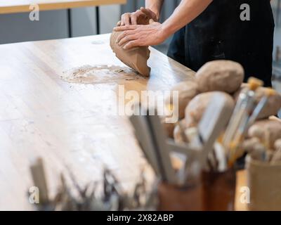 Un potier pétrit l'argile avant de l'utiliser dans l'atelier. Gros plan des mains d'un homme. Banque D'Images