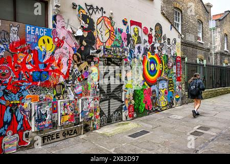 Montage vibrant d'autocollants Street art sur un mur, « LA PAIX COMMENCE AVEC Un SOURIRE » et « GAZA LIBRE » se démarquent, indiquant un mélange d'images ludiques et de p Banque D'Images