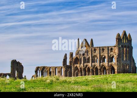 Une abbaye historique, partiellement en ruine à l'architecture gothique, située sur une colline herbeuse sous un ciel bleu avec des nuages tortueux. Banque D'Images