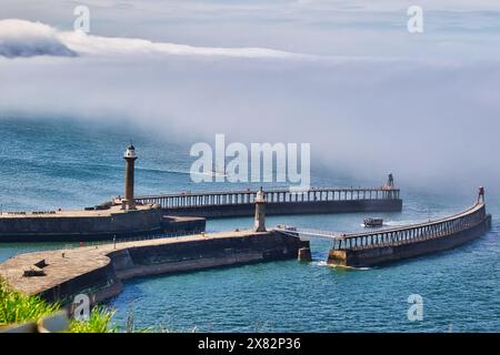 Vue aérienne d'un port côtier avec deux jetées s'étendant dans la mer, chacune avec un phare à l'extrémité. Un bateau navigue au loin, et là Banque D'Images