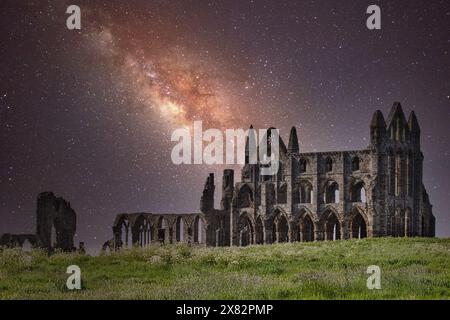 Une vue nocturne d'une ancienne abbaye en ruines avec la galaxie de la voie lactée visible dans le ciel étoilé au-dessus. L'abbaye est située sur un champ herbeux. Banque D'Images