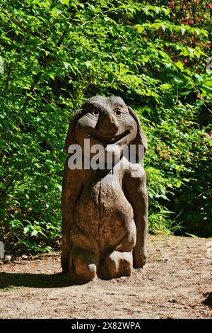 Sculpture en bois d'un personnage de dessin animé souriant avec une grande tête et un corps court, placée à l'extérieur dans une zone boisée. Banque D'Images