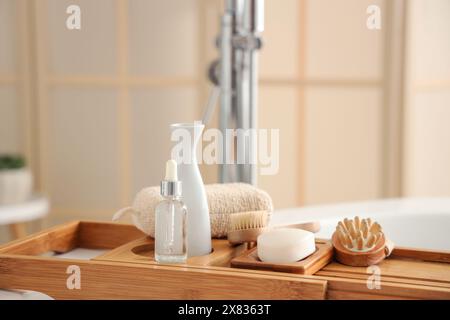 Plateau de bain en bois avec différentes fournitures et produits cosmétiques dans la salle de bains lumineuse Banque D'Images