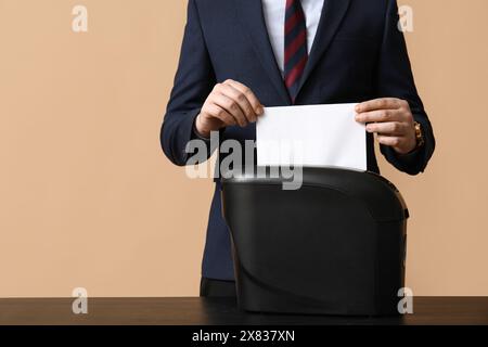 Jeune homme détruisant la feuille de papier dans la déchiqueteuse sur fond brun, gros plan Banque D'Images