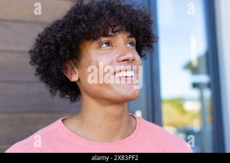 Un jeune homme biracial portant une chemise rose, souriant dehors Banque D'Images