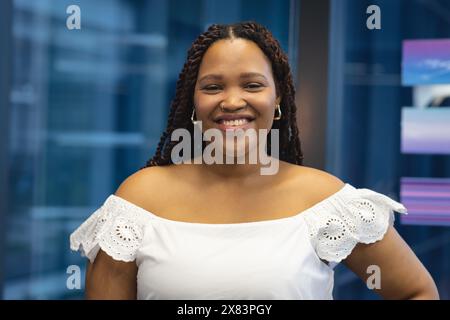 Au bureau moderne pour les affaires, jeune femme biraciale debout à l'intérieur, souriant à la caméra Banque D'Images