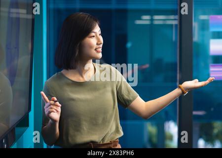 Au bureau moderne pour les affaires, jeune femme asiatique présentant, pointant à l'écran Banque D'Images