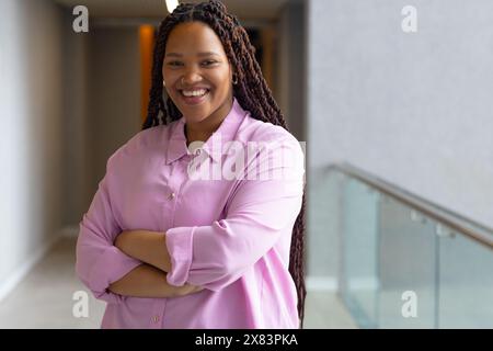 Jeune femme biraciale se tient confiante dans le bureau moderne pour le couloir d'affaires, souriant Banque D'Images