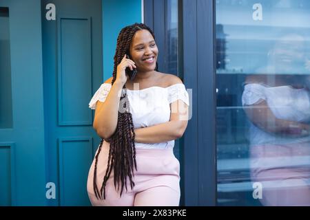 Jeune femme biraciale parle sur smartphone près d'un bureau moderne pour les affaires Banque D'Images