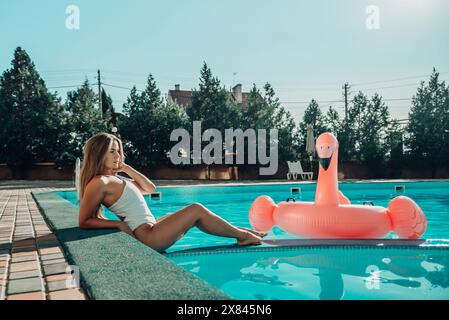 Une femme est allongée dans une piscine avec un flotteur rose flamant rose. La scène est relaxante et amusante, avec la femme profitant de son temps dans l'eau. Banque D'Images